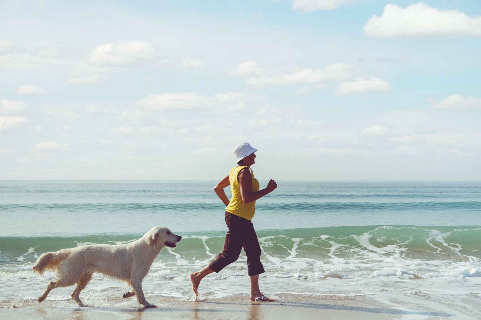 Eine Frau und ein Hund laufen am Strand.