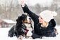 Eine Frau spielt mit ihrem Hund im Schnee.