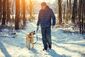 Ein Mann spaziert mit seinem Hund im Wald durch den Schnee.