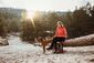 Hanna Busch in Wanderkleidung sitzt neben ihrem Hund in den Bergen auf einem Baumstamm.