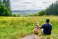 Mann und Hund sitzen nebeneinander auf einer Wiese und schauen in die Ferne.