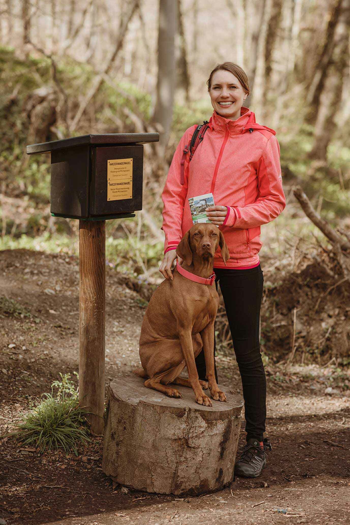 Hanna Busch in Wanderkleidung mit Hund vor einem Harzer Stempelkasten.