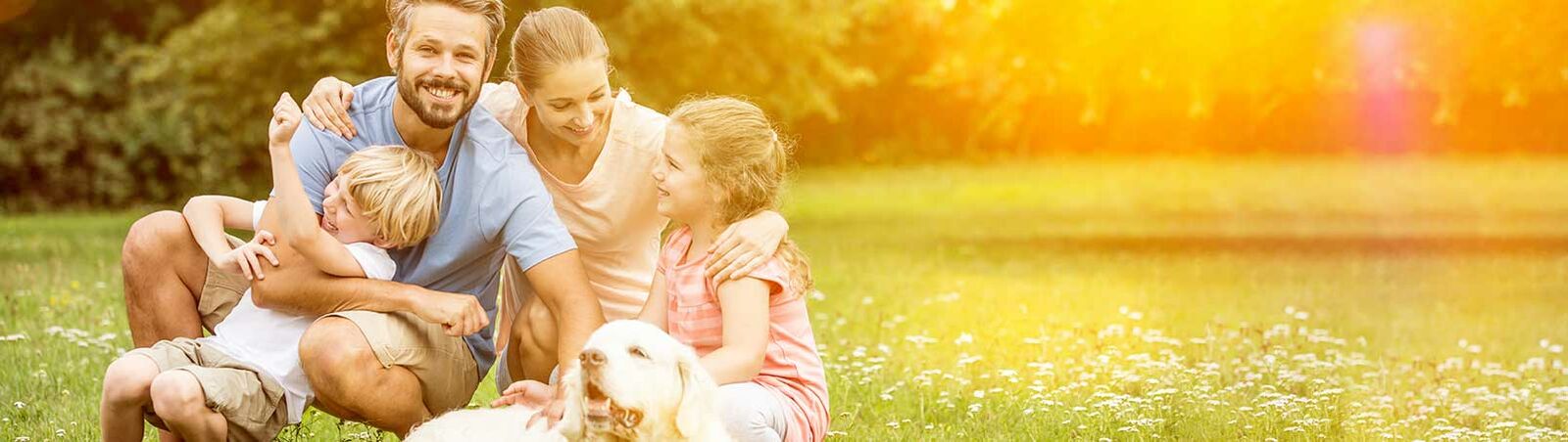 Eine Familie, bestehend aus Mutter, Vater und zwei Kindern, sitzt mit ihrem Hund auf einer Wiese.