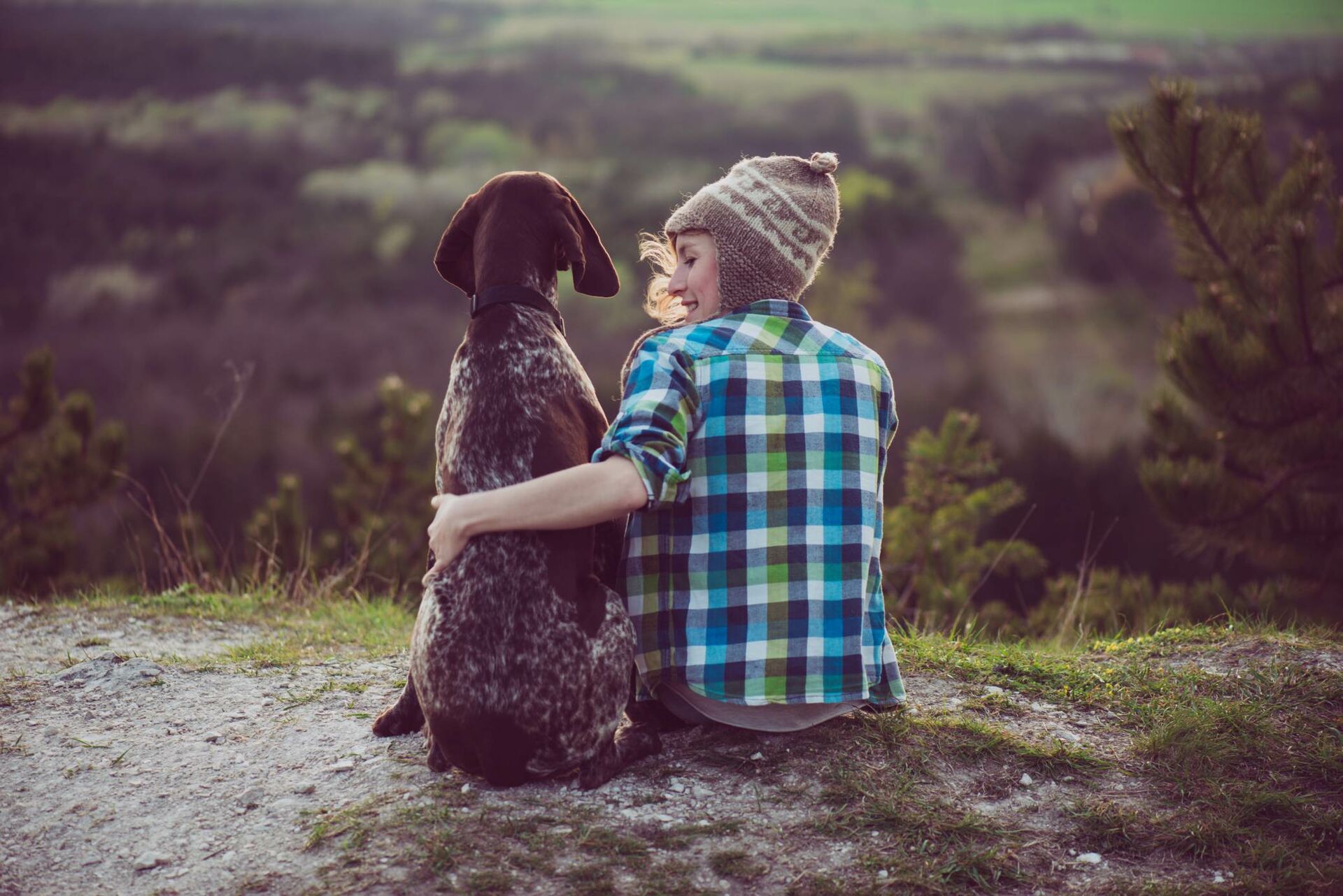 Ein großer dunkelbrauener Hund sitzt neben seiner Besitzerin und sie legt den Arm um sie.