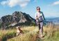 Eine lachende Frau joggt mit ihrem Beagle in einer Berglandschaft.