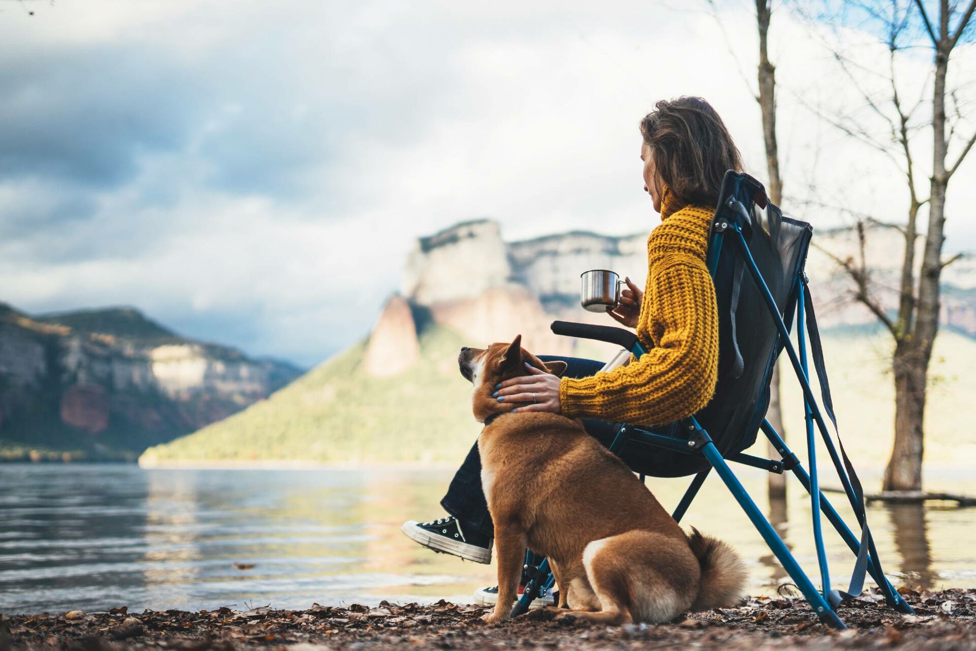 Ein Mann sitzt auf einem Campingstuhl und streichelt seinen Hund, der neben dem Stuhl sitzt.