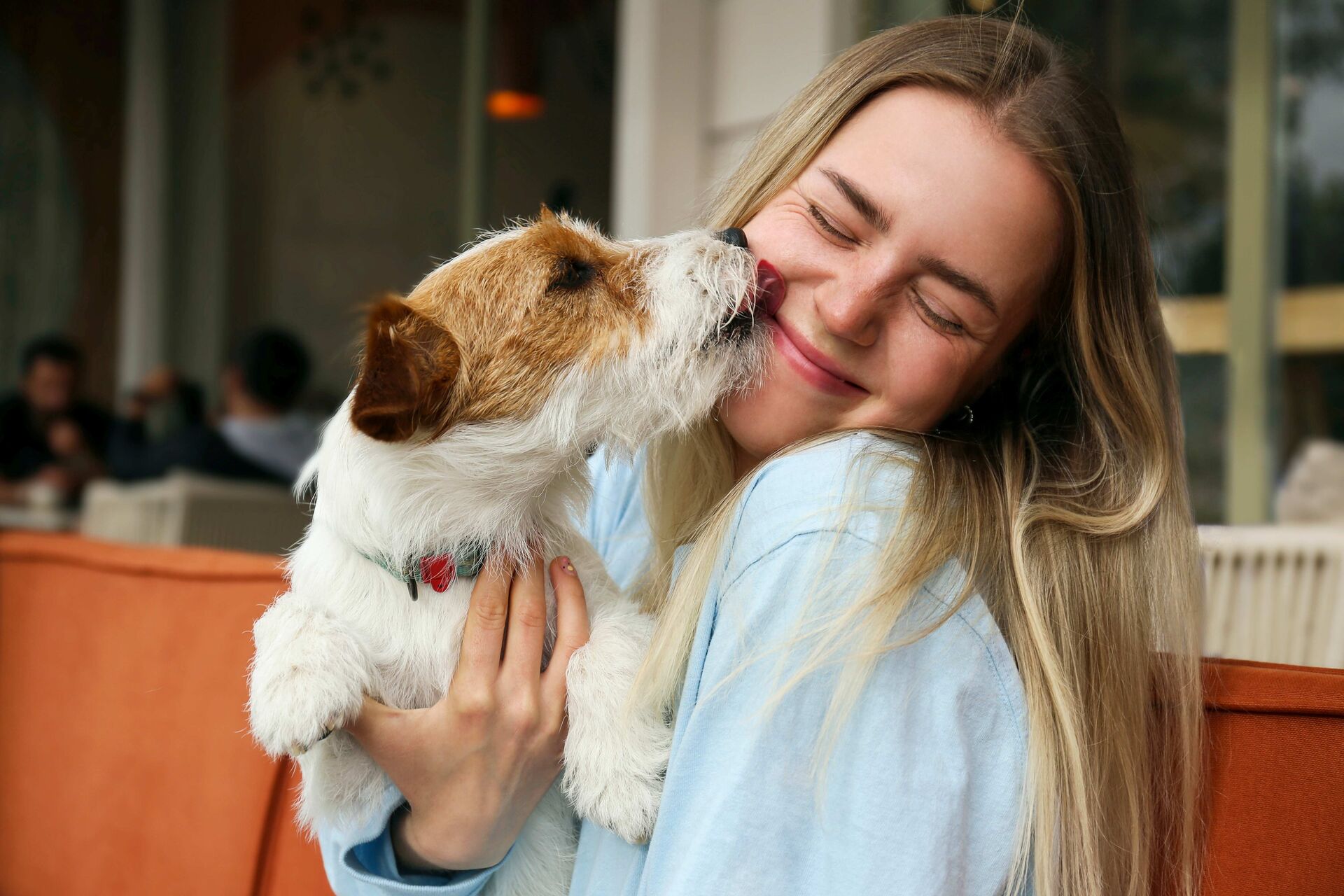 Eine Frau trägt einen Hund auf dem Arm. Der Hund leckt das Gesicht der Frau ab.