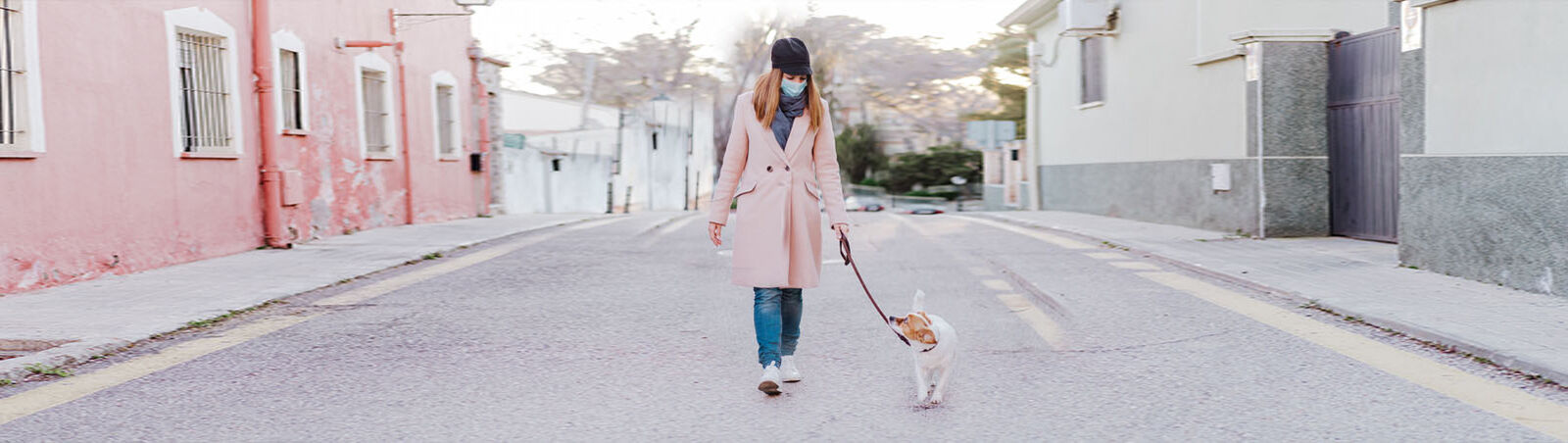 Hund und Halterin mit weißer Atemschutzmaske spazieren durch die Stadt.