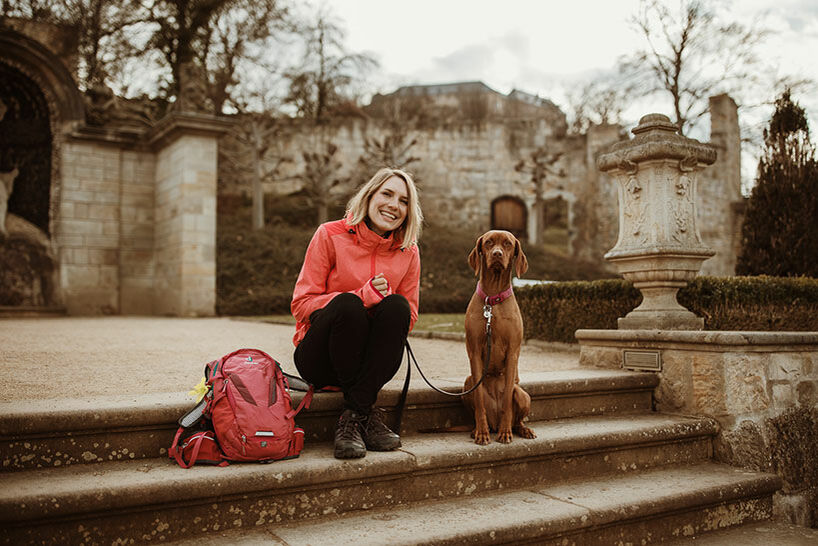 Hanna Busch in Wanderkleidung sitzt neben ihrem Hund auf einer Schlosstreppe.
